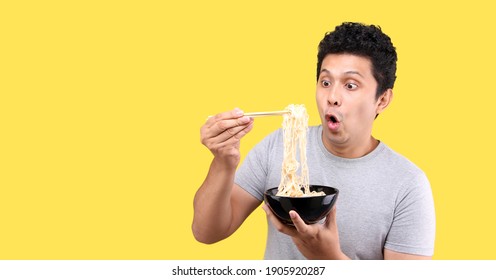 Close Up Asian Man Eating Yummy Hot And Spicy Instant Noodle Using Chopsticks And Bowl Isolated On Yellow Background In Studio With Copy Space.