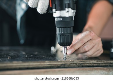 Close up asian man hand holding electric cordless screwdriver machine and screws lie for screwing a screw assembling furniture at home. iron screw, screws as a background, wood screw, concept industry