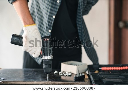 Close up asian man hand holding electric cordless screwdriver machine and screws lie for screwing a screw assembling furniture at home. iron screw, screws as a background, wood screw, concept industry