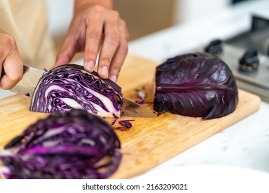 Close up of Asian man hand using knife cutting fresh red cabbage on cutting board in the kitchen at home. Happy female enjoy cooking and having dinner eating healthy food on holiday vacation - Powered by Shutterstock