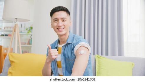 Close Up Of Asian Man Has Coronavirus Vaccine And Show His Arm In Living Room At Home - Thumb Up Gesture