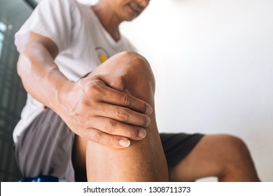 Close up of an asian man holding his knee in pain