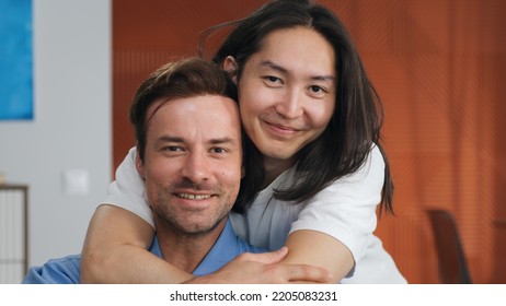 Close Up Of Asian Man Hug Boyfriend From Behind Sitting On Couch. Happy Diverse Homosexual Male Couple Embrace And Smile At Camera