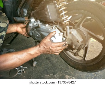 Close Up Asian Mechanic's Hands Detaching Engine Cover Of The Old Motorcycle For Repairing With Flare Light At Workshop, 