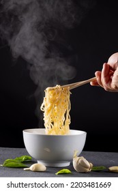 Close Up Of Asian Noodles Held In Chopsticks By Caucasian Man On Black Background. Asian Tasty Home Cooked Food And Healthy Eating.