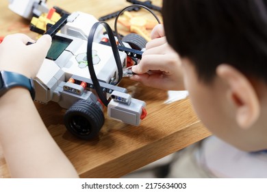 Close up of Asian student child's hands and face connecting cable  to vehicle robot, testing and solving engineering problem on table. STEM education and 21st century learning skills concept - Shutterstock ID 2175634003