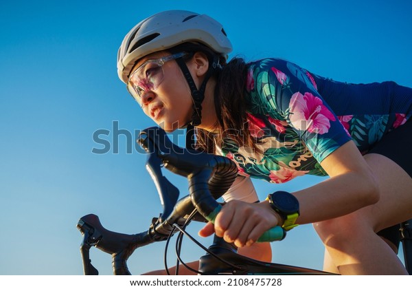 close up asian woman\
with athletic body shape in protective helmet and glasses riding\
bicycle on blue sky 