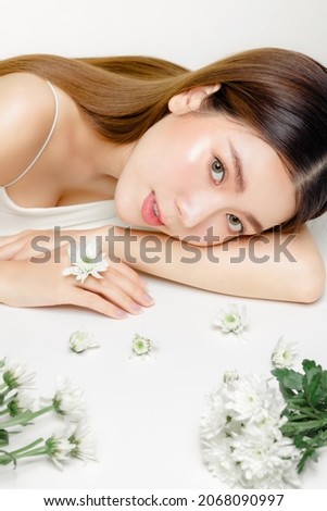 Close up of Asian woman with a beautiful face and fresh, smooth skin and flower. Cute female model with natural makeup and sparkling eyes is looking at the camera on white isolated background.