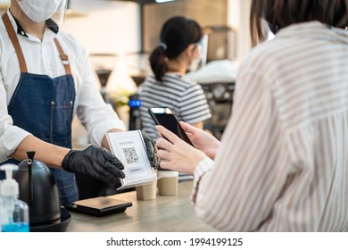 Close up of Asian woman customer make a quick and easy contactless payment in cafe during Covid19 Pandemic. Young girl use smartphone Scanning QR code to pay for service and drink from barista waiter. - Powered by Shutterstock