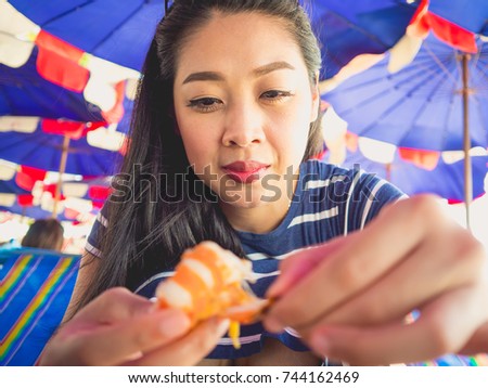 Close up of Asian woman eating local grilled seafood of Thailand beach.