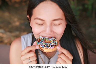 Close Up Asian Woman Eating Rainbow Donut.