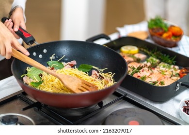 Close Up Of Asian Woman Hand Cooking Healthy Food Pasta And Salmon Steak On Cooking Pan In The Kitchen At Home. Happy Female Having Dinner Party Meeting Celebration With Friends On Holiday Vacation