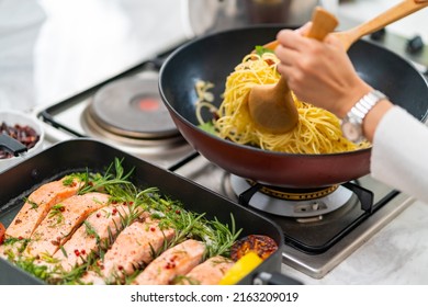 Close Up Of Asian Woman Hand Cooking Healthy Food Pasta And Salmon Steak On Cooking Pan In The Kitchen At Home. Happy Female Having Dinner Party Meeting Celebration With Friends On Holiday Vacation