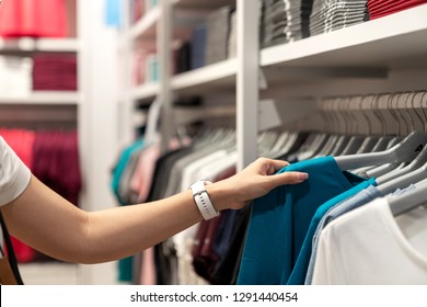 Close Up Of Asian Woman Hand Shopping Or Choosing Casual Blue Color T-shirt On Rack At Young Clothes Shop At Department Store. Customer In Retail Unisex Shirt Business Store With Summer Sale Concept.