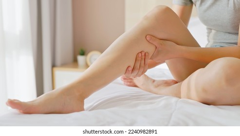 close up of asian woman hand touch massage her calf on bed in bedroom at home - she has leg cramp muscle pain