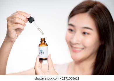 Close Up Asian Woman Looks At A Bottle Of CBD Oil. Sleep Supplement. Medical Marijuana. Vitamins And Supplements Healthy Alternatives.
