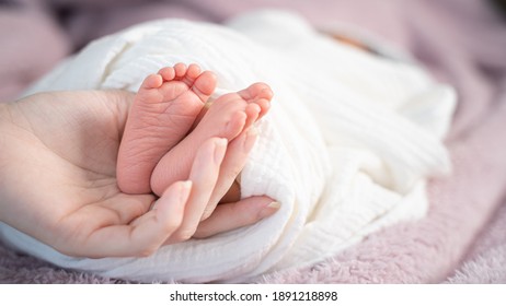 Close Up Asian Woman Mother Hand Holding Small Baby Infant Feet While Sleeping On Soft Bed Covered With White Cloth.