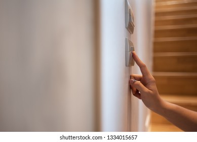 Close Up Of Asian Woman Right Hand Is Turning On Or Off On Light Switch Over Wooden Stair Background. Copy Space.