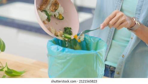 close up of asian woman scraping food leftovers or waste into kitchen bucket at home