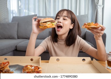 Close up asian woman takeaway eating junk food hamburger and pizza close-up shot in living room at home,  Fast food delivery service safe and stop coronavirus spread by social distancing concept.