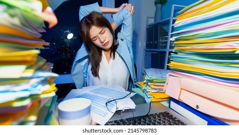 close up of asian young businesswoman has shoulder pain while working overtime with laptop and documents and she is stretching her arms in office - Shutterstock ID 2145798783