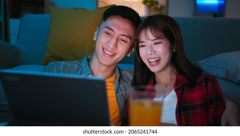 close up of asian young couple are watching movie or video by digital tablet and sitting on the floor happily with juice at night in living room