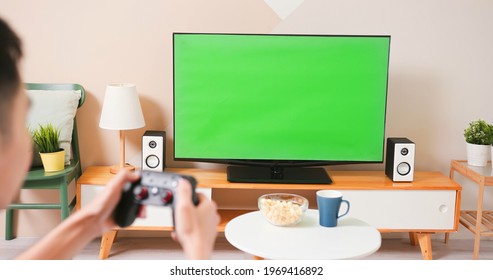 Close Up Of Asian Young Gamer Boy Sitting On Couch Holding Wireless Controller Playing Video Games On A Green Chroma Key TV Screen At Home