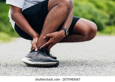 Close Up Asian Young Sport Runner Black Man Wear Watch Hands Joint Hold Leg Pain Because Of Twisted Ankle Broken While Running At The Outdoor Street Health Park, Healthy Exercise Injury From Workout