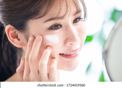 close up of asian young woman look in mirror and apply moisturized cream or sunscreen on her face