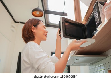 Close Up Asian Young Woman Opening Microwave Oven To Lay Dish Of Food For Defrost In The Kitchen At Home For Comfortable Lifestyle Concept