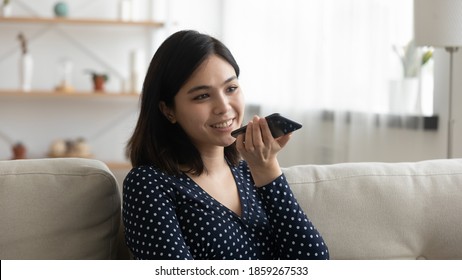 Close Up Asian Young Woman Recording Voice Message On Phone, Sitting On Couch At Home, Positive Attractive Female Holding Smartphone Near Mouth, Speaking, Making Call By Speakerphone, Chatting