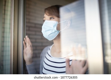 close up of asian young woman wearing face mask stay isolation at home for self quarantine due to epidemic of COVID19 - she looks out the window - Powered by Shutterstock