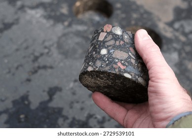 Close up of asphalt core sample held in a human hand during road inspection. Concept of construction quality control, infrastructure maintenance, pavement testing, engineering analysis and urban road repair