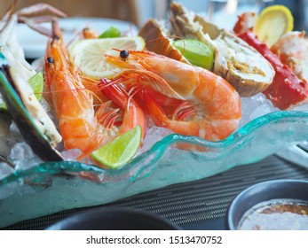 Close Up Assorted Fresh Cooked Cold Seafood As Shrimps, Prawns, New Zealand Mussels, Mussels, Oyster, Rock Lobster, Lobster Claw With Yello Leomon In Oval Shaped Dish Or Plate On Ice On Wooden Table