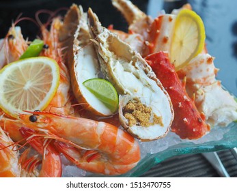 Close Up Assorted Fresh Cooked Cold Seafood As Shrimps, Prawns, New Zealand Mussels, Mussels, Oyster, Rock Lobster, Lobster Claw With Yello Leomon In Oval Shaped Dish Or Plate On Ice On Wooden Table