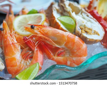 Close Up Assorted Fresh Cooked Cold Seafood As Shrimps, Prawns, New Zealand Mussels, Mussels, Oyster, Rock Lobster, Lobster Claw With Yello Leomon In Oval Shaped Dish Or Plate On Ice On Wooden Table