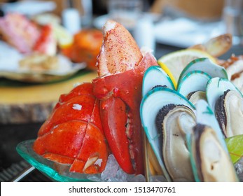 Close Up Assorted Fresh Cooked Cold Seafood As Shrimps, Prawns, New Zealand Mussels, Mussels, Oyster, Rock Lobster, Lobster Claw With Yello Leomon In Oval Shaped Dish Or Plate On Ice On Wooden Table