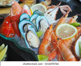 Close Up Assorted Fresh Cooked Cold Seafood As Shrimps, Prawns, New Zealand Mussels, Mussels, Oyster, Rock Lobster, Lobster Claw With Yello Leomon In Oval Shaped Dish Or Plate On Ice On Wooden Table