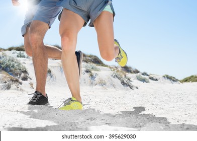 Close up of athletic runners legs running on beach. Sporty fit couple jogging on sand during outdoor workout. Human legs running on sandy beach, copy space.