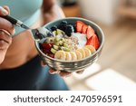 Close up of athletic woman eating a healthy fruit bowl in the kitchen at home