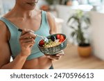 Close up of athletic woman eating a healthy fruit bowl in the kitchen at home