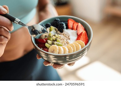 Close up of athletic woman eating a healthy fruit bowl in the kitchen at home