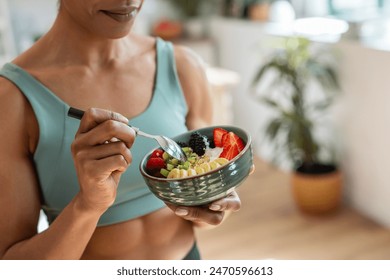 Close up of athletic woman eating a healthy fruit bowl in the kitchen at home