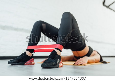 Close up of athletic woman in squat together in gym. Fit girl is exercising with resistance band for lower body relief. She is wearing sport clothes and sneakers