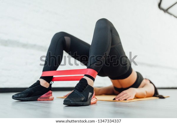 Close up of athletic\
woman in squat together in gym. Fit girl is exercising with\
resistance band for lower body relief. She is wearing sport clothes\
and sneakers
