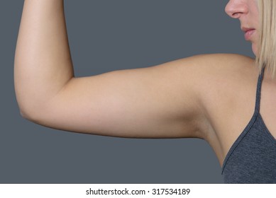 Close Up Athletic Young Woman Showing Her Arm Muscle Against Grey Wall Background.