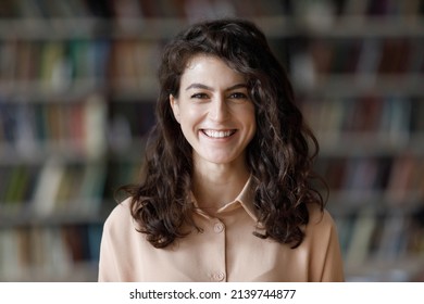 Close up attractive brunette teenage girl with curly hair pose in library look at camera, head shot portrait on bookshelves background. Higher education institution student, excellent studies concept - Shutterstock ID 2139744877