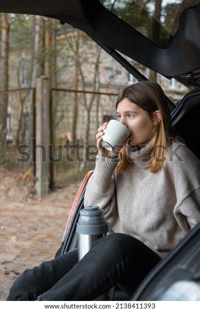 Close up of\
attractive girl sitting in car trunk and drinking beverage from\
cup. Travelling by car. Freedom\
concept.