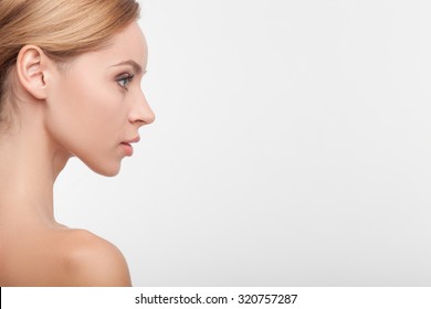 Close up of attractive girl standing in profile. She is looking forward with confidence. Her shoulders are naked. Isolated and copy space in right side