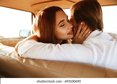 Close up of an attractive happy couple in love kissing while sitting together inside a retro car on a front seat